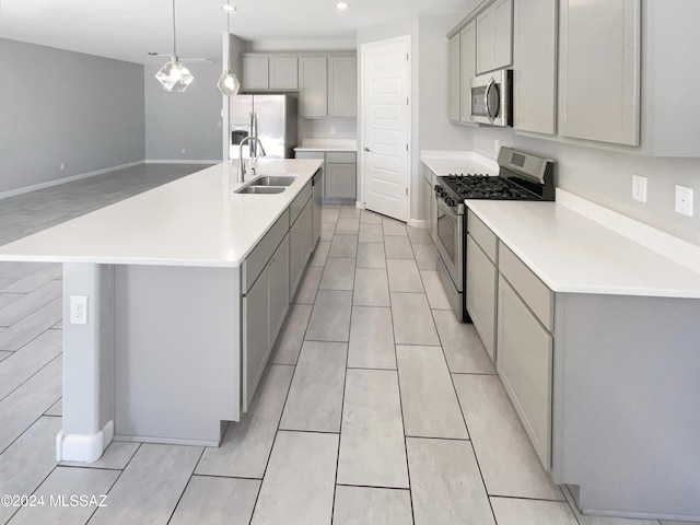 kitchen featuring gray cabinets, light countertops, appliances with stainless steel finishes, a kitchen island with sink, and a sink