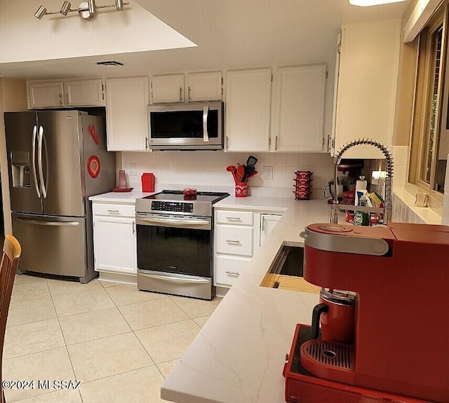 kitchen featuring white cabinets, stainless steel appliances, light tile patterned floors, and tasteful backsplash