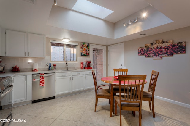 kitchen with dishwasher, light tile patterned flooring, range, white cabinetry, and a skylight