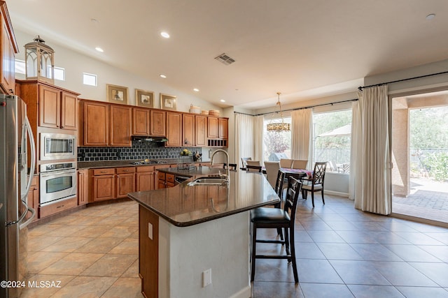 kitchen with a center island with sink, sink, hanging light fixtures, tasteful backsplash, and stainless steel appliances