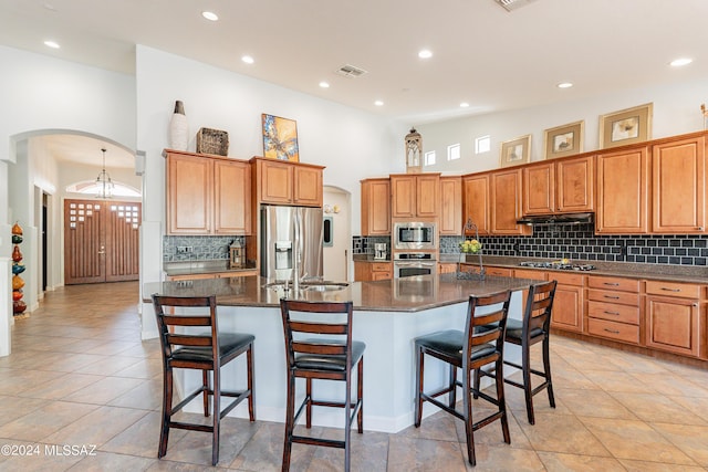 kitchen with a kitchen breakfast bar, stainless steel appliances, high vaulted ceiling, and a kitchen island with sink