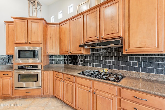 kitchen featuring decorative backsplash, light tile patterned flooring, dark stone countertops, and appliances with stainless steel finishes