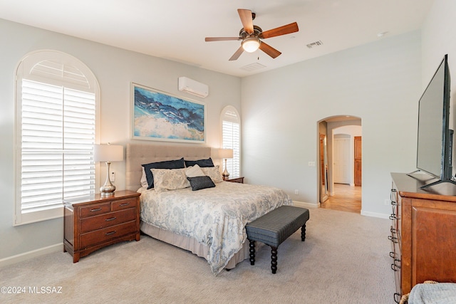 bedroom with ceiling fan, light colored carpet, and an AC wall unit