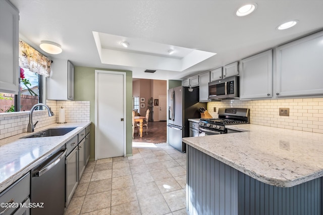 kitchen featuring a raised ceiling, appliances with stainless steel finishes, sink, gray cabinets, and decorative backsplash