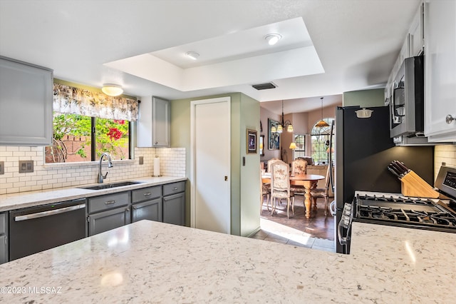 kitchen featuring backsplash, sink, hanging light fixtures, appliances with stainless steel finishes, and gray cabinetry