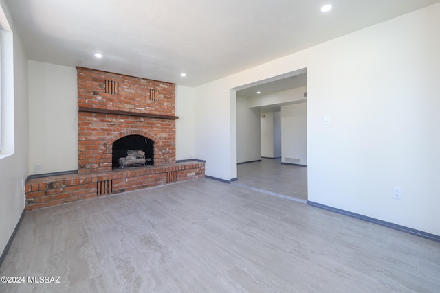 unfurnished living room with a brick fireplace and light hardwood / wood-style floors