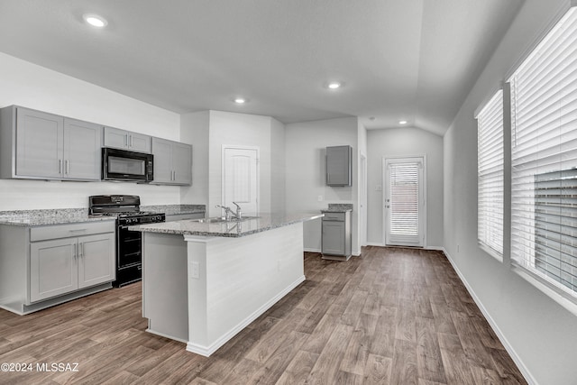 kitchen with vaulted ceiling, a center island with sink, black appliances, wood-type flooring, and gray cabinets