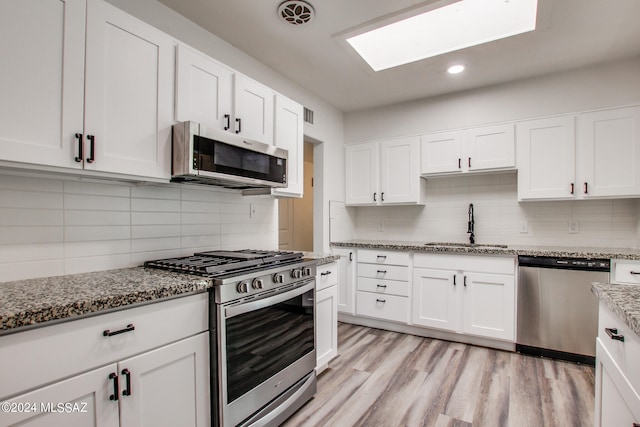 kitchen with stainless steel appliances, sink, light stone countertops, white cabinets, and light hardwood / wood-style floors