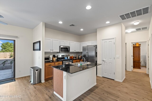 kitchen with white cabinets, light hardwood / wood-style flooring, appliances with stainless steel finishes, sink, and a center island with sink