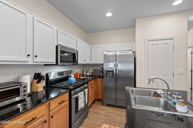 kitchen featuring dark stone counters, light hardwood / wood-style flooring, stainless steel appliances, sink, and white cabinets