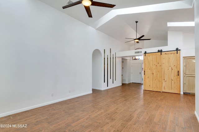 unfurnished living room with high vaulted ceiling, ceiling fan, hardwood / wood-style floors, and a barn door