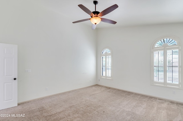 carpeted empty room with a wealth of natural light, a towering ceiling, and ceiling fan