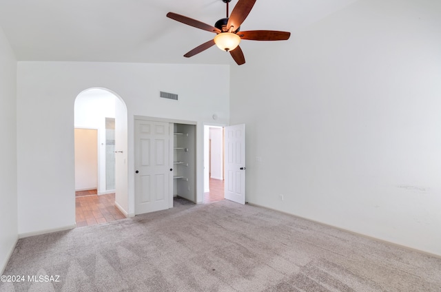 unfurnished bedroom with ceiling fan, light colored carpet, a closet, and high vaulted ceiling