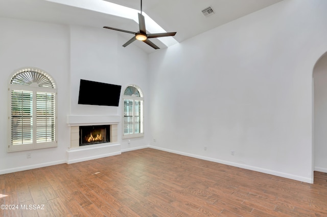 unfurnished living room with a tile fireplace, hardwood / wood-style flooring, ceiling fan, and high vaulted ceiling