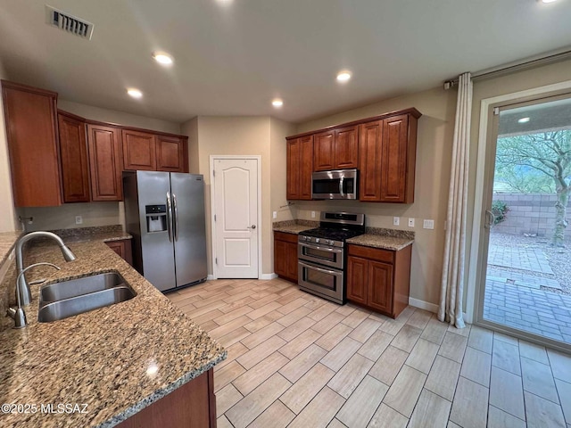 kitchen with visible vents, stone counters, stainless steel appliances, and a sink