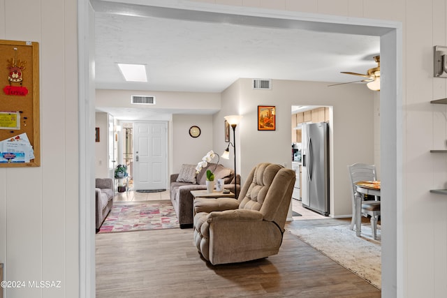 living room with ceiling fan, a skylight, and light hardwood / wood-style floors