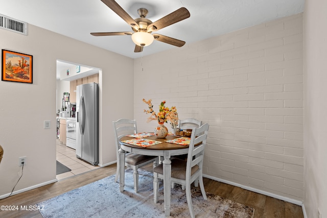 dining room with light wood-type flooring, brick wall, and ceiling fan