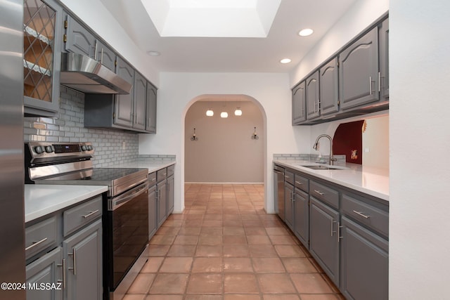 kitchen with tasteful backsplash, a skylight, light tile patterned floors, stainless steel appliances, and sink