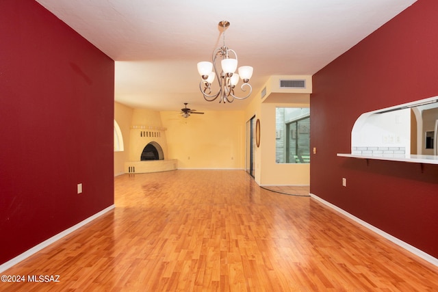 spare room with ceiling fan with notable chandelier, a fireplace, and light hardwood / wood-style floors