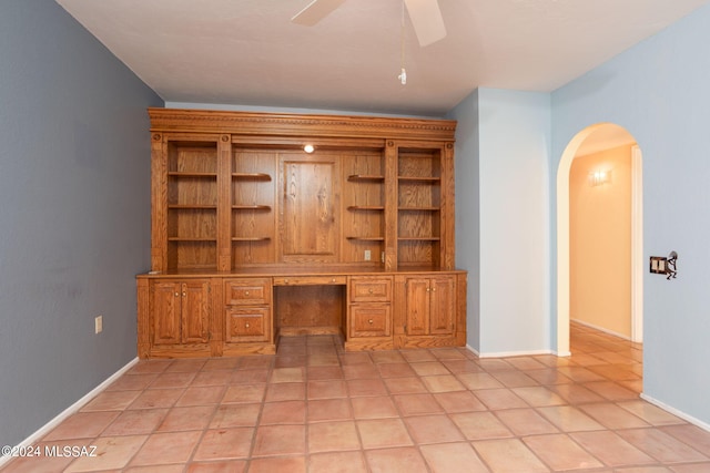 unfurnished office with built in desk, ceiling fan, and light tile patterned floors