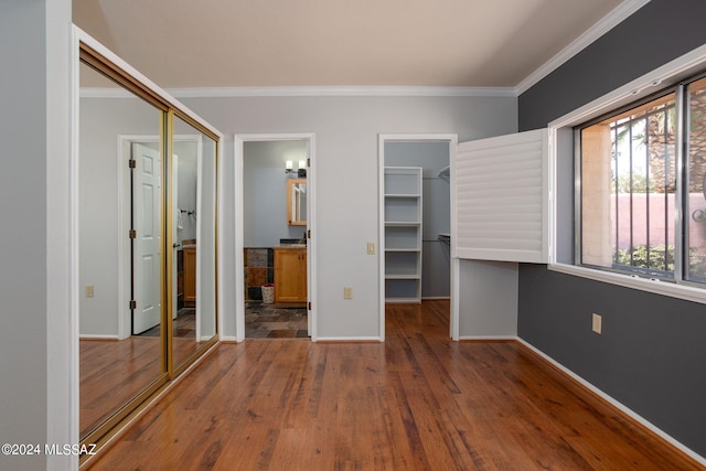 unfurnished bedroom featuring a spacious closet, a closet, wood-type flooring, crown molding, and connected bathroom