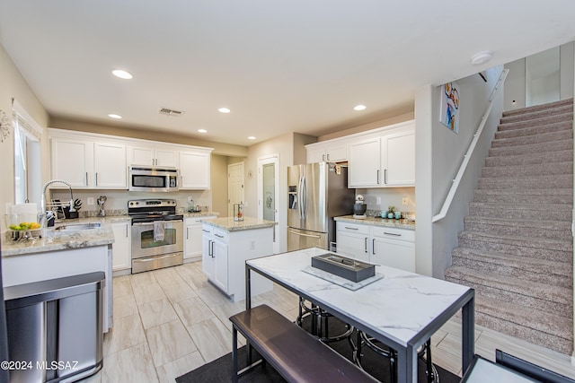 kitchen with visible vents, a kitchen island, stainless steel appliances, white cabinetry, and a sink