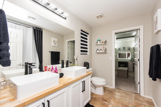 bathroom with toilet, double vanity, visible vents, and a sink