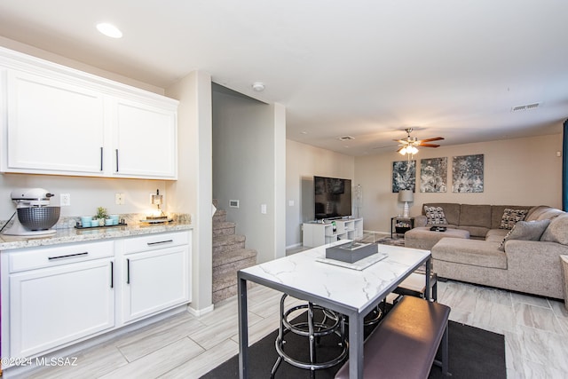 interior space featuring ceiling fan, visible vents, white cabinets, open floor plan, and light stone countertops