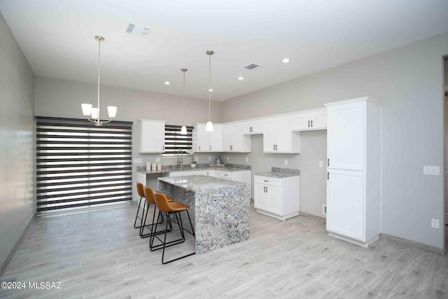 kitchen featuring light stone counters, sink, white cabinetry, hanging light fixtures, and a kitchen island