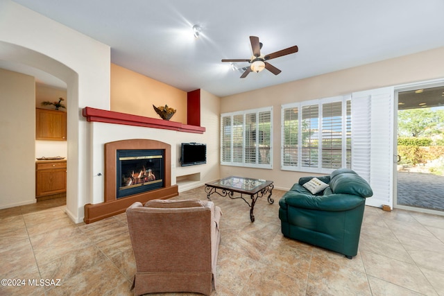 living room featuring ceiling fan, baseboards, a glass covered fireplace, and light tile patterned floors