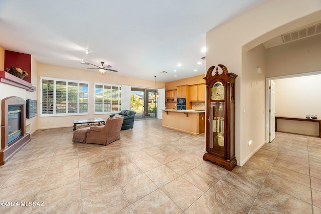 living area featuring a ceiling fan, visible vents, recessed lighting, arched walkways, and a glass covered fireplace