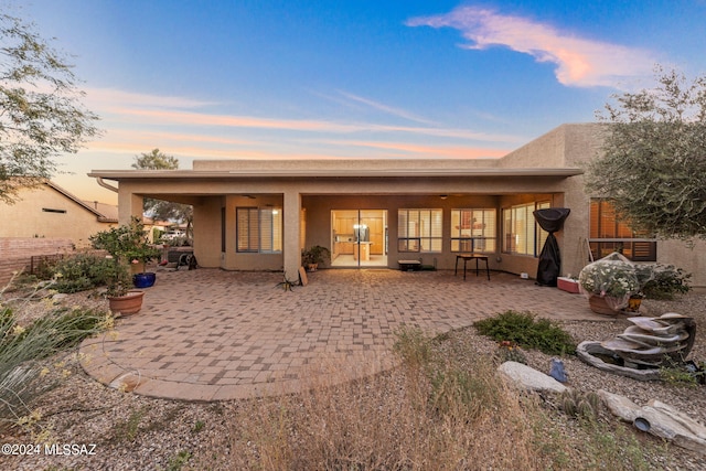 back of house at dusk with stucco siding and a patio