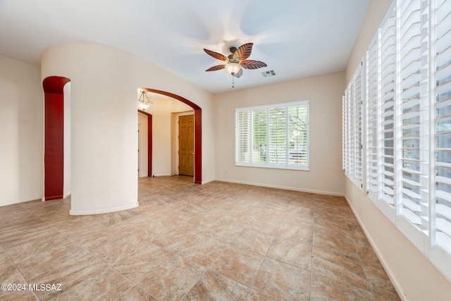 unfurnished room featuring visible vents, arched walkways, baseboards, and ceiling fan