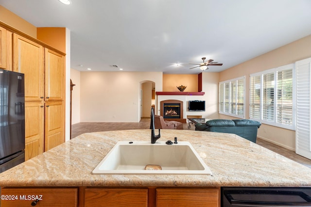 kitchen featuring light stone countertops, freestanding refrigerator, a lit fireplace, a sink, and open floor plan