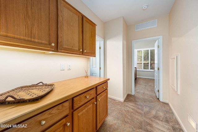 hallway featuring visible vents, stone finish flooring, and baseboards