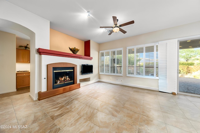 unfurnished living room featuring a glass covered fireplace, light tile patterned flooring, a ceiling fan, and baseboards