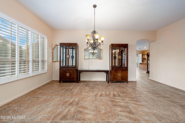 unfurnished dining area featuring a notable chandelier, baseboards, and arched walkways