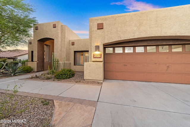 pueblo-style home featuring concrete driveway, a garage, and stucco siding