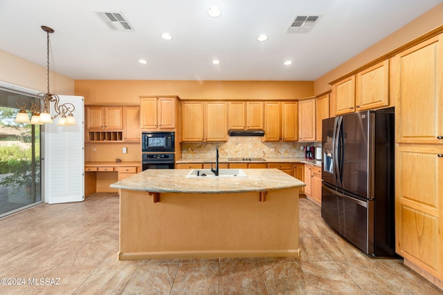 kitchen featuring visible vents, black appliances, a center island with sink, a sink, and light stone countertops