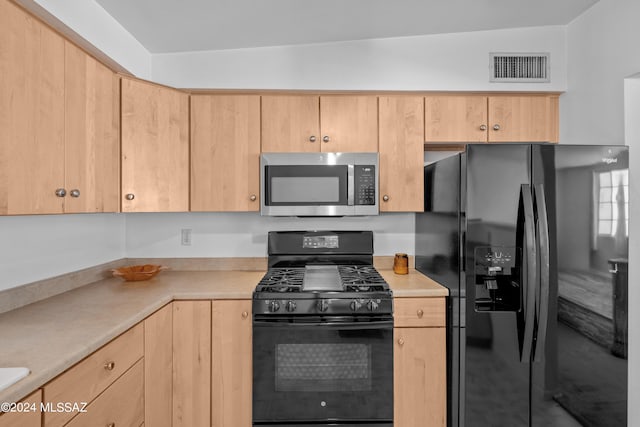 kitchen featuring black appliances, light brown cabinetry, and vaulted ceiling