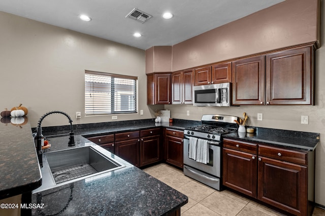 kitchen featuring dark stone countertops, dark brown cabinets, stainless steel appliances, and sink