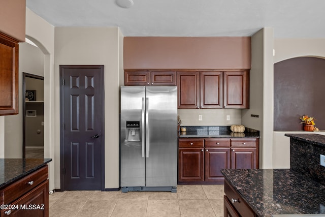 kitchen with dark stone countertops, light tile patterned floors, and stainless steel refrigerator with ice dispenser