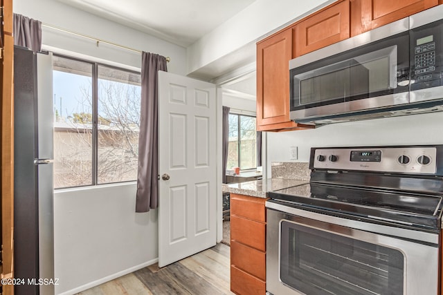 kitchen with appliances with stainless steel finishes, stone counters, and light hardwood / wood-style flooring