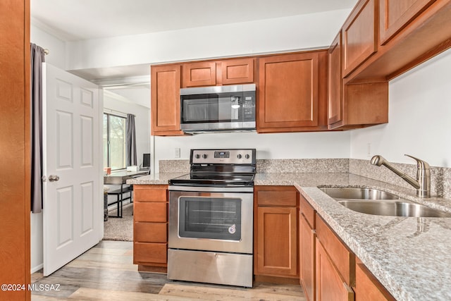 kitchen featuring appliances with stainless steel finishes, light stone countertops, sink, and light hardwood / wood-style flooring