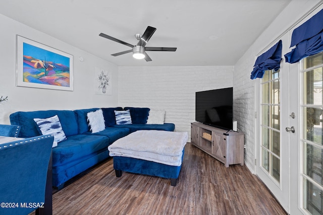 living room with brick wall, dark wood-type flooring, and ceiling fan