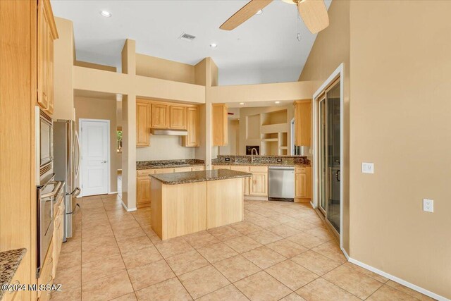 kitchen with ceiling fan, a kitchen island, high vaulted ceiling, appliances with stainless steel finishes, and light brown cabinetry