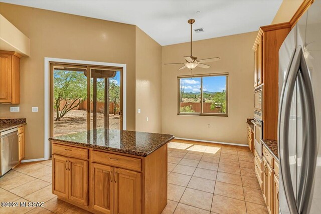 kitchen with ceiling fan, appliances with stainless steel finishes, dark stone counters, and a healthy amount of sunlight