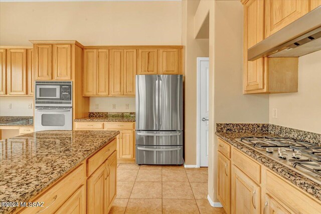 kitchen featuring light brown cabinetry, stainless steel appliances, extractor fan, and stone countertops