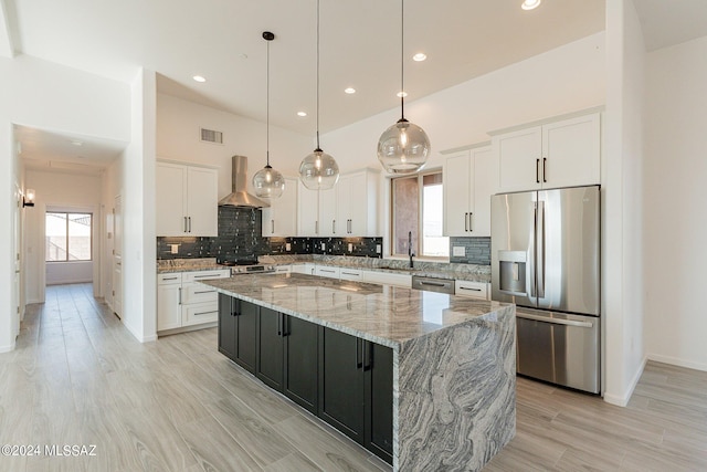 kitchen with appliances with stainless steel finishes, white cabinetry, wall chimney exhaust hood, pendant lighting, and a kitchen island