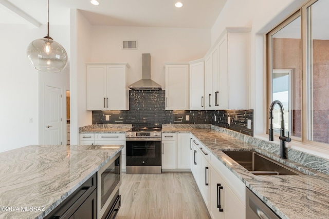 kitchen with light hardwood / wood-style flooring, appliances with stainless steel finishes, white cabinetry, sink, and wall chimney exhaust hood